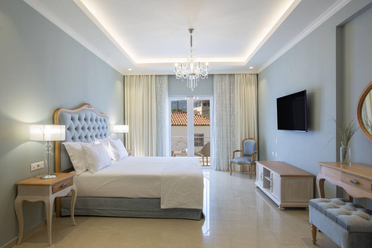 Een moderne hotelkamer met een groot bed, een kroonluchter, een televisie en uitzicht op het omliggende landschap.