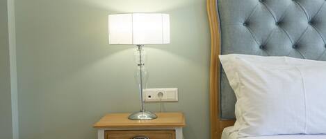 A neatly made bed with a tufted headboard, a bedside table with a lamp, and a drawer.