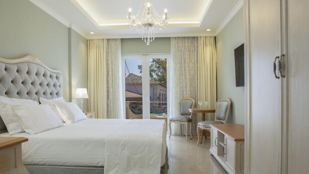 Ruime slaapkamer met een groot bed, een kroonluchter, een zithoek met een tafel en stoelen, en uitzicht door een glazen deur.