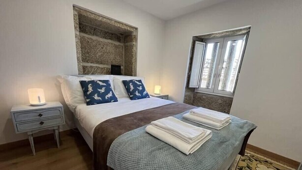 Un dormitorio con cama, mesitas de noche, una ventana y un tapete estampado.