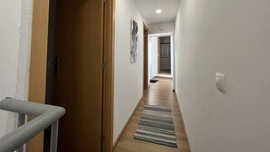 Un pasillo estrecho con puertas de madera, una alfombra estampada y una lámpara en el techo.