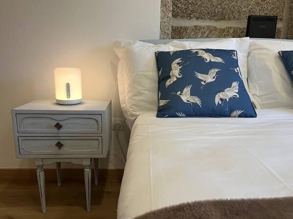 A neatly made bed with white and blue pillows, a bedside lamp, and a small white nightstand with drawers. - Vila Mena by Trip2Portugal (Guarda)