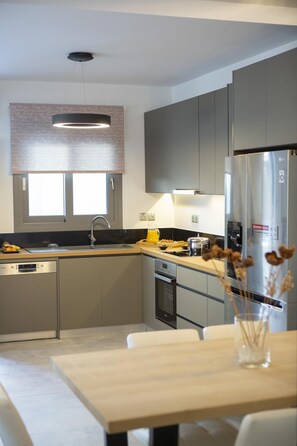 Eine moderne Küche mit grauen Schränken, einem Edelstahl-Kühlschrank, einem eingebauten Backofen und einem Geschirrspüler.