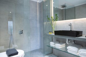 Ein modernes Badezimmer mit Duschkabine aus Glas, Toilette, schwarzem Waschbecken auf einer Glasablage und ordentlich gefalteten weißen Handtüchern.