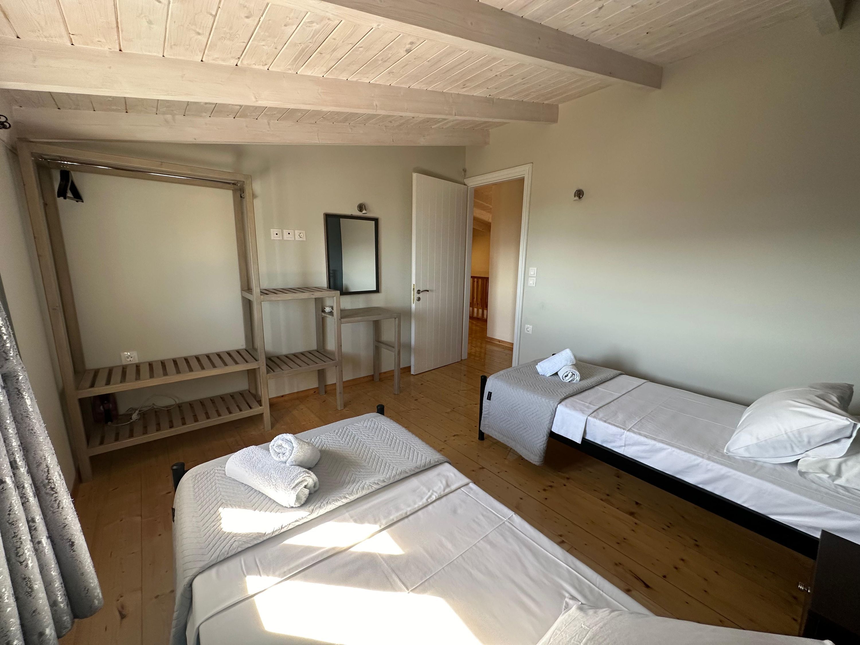 A room with two beds, a wooden desk, a mirror, and a wardrobe.