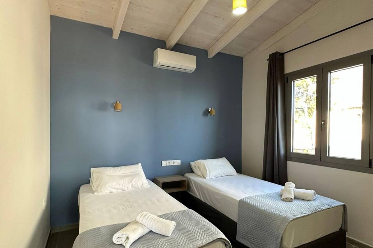 A room with two beds, an air conditioning unit, a window with curtains, and a hanging light fixture.