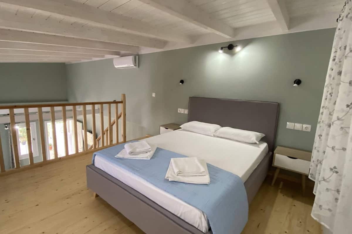 A bedroom with a bed, bedside tables, a nightstand, a wooden railing, and an air conditioning unit.