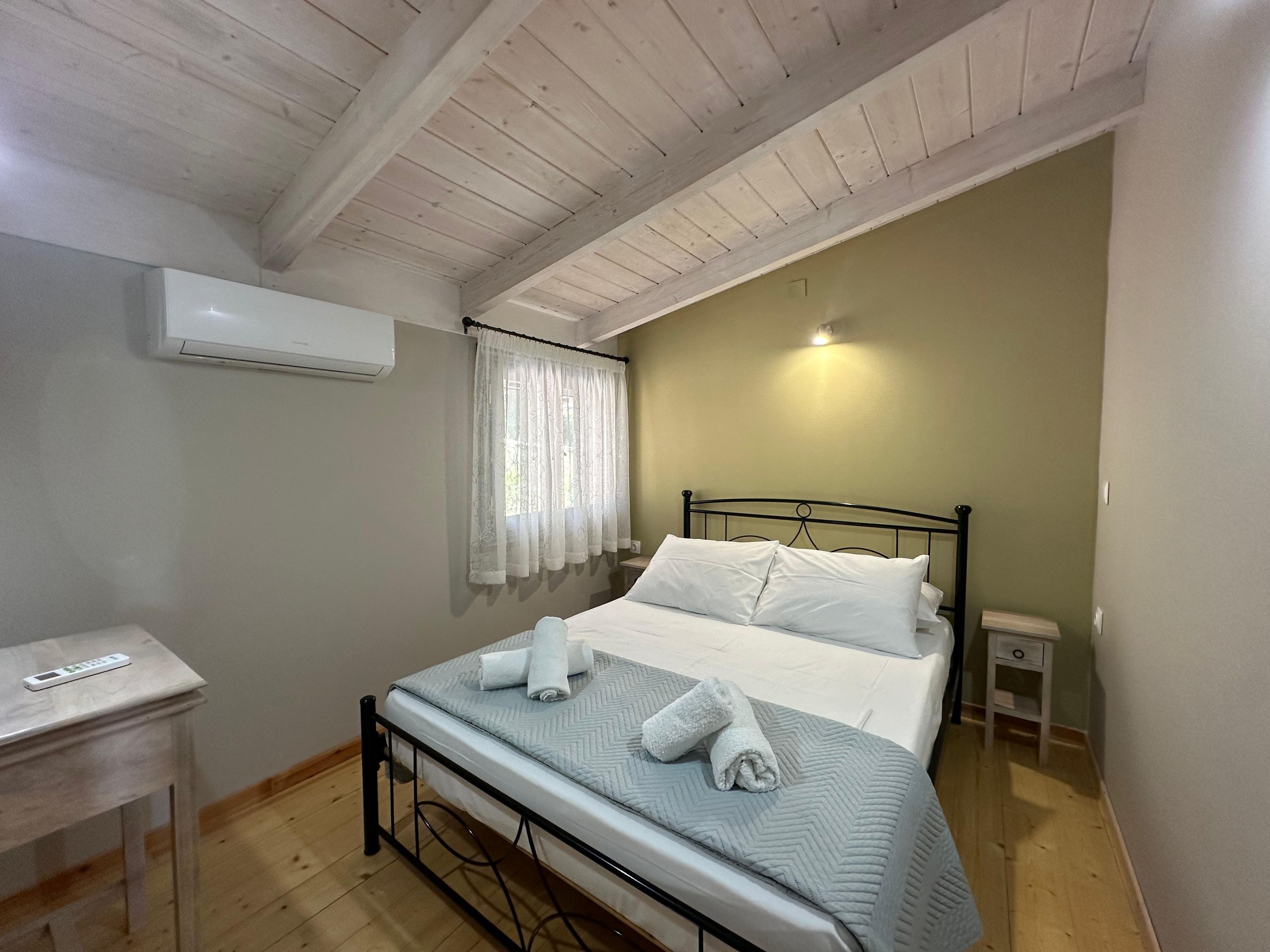 A bedroom with a bed, a bedside table, a nightstand, an air conditioning unit, and a window with curtains.