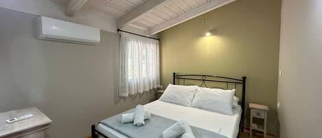 A bedroom with a bed, a bedside table, a nightstand, an air conditioning unit, and a window with curtains.
