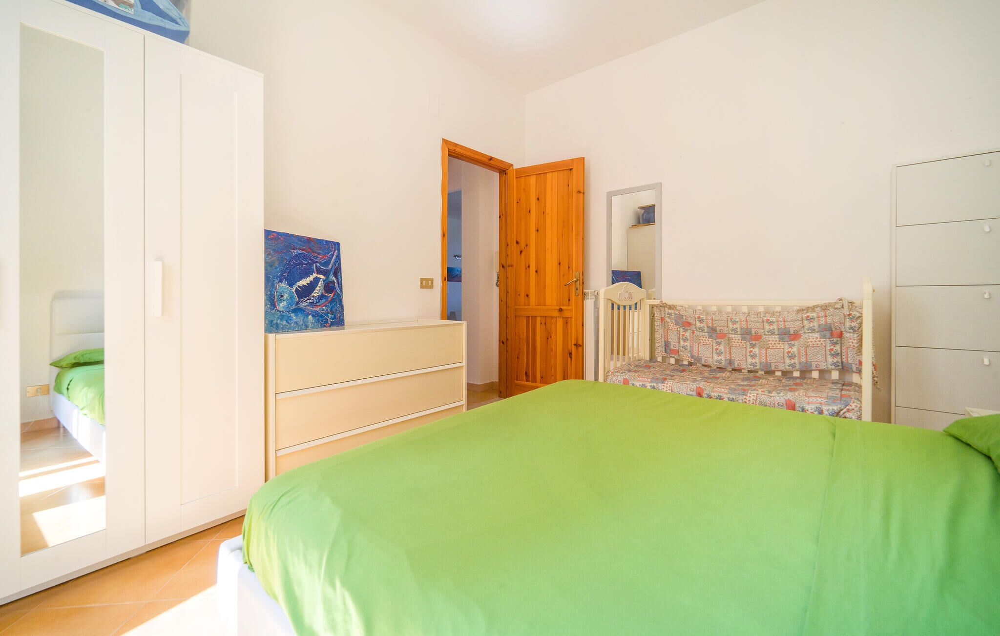 A bedroom with a bed, a wardrobe, a crib, and a door leading to another room.