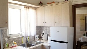 Una cocina compacta con un refrigerador blanco, estufa, lavamanos y una ventana con cortinas.