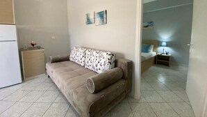 A compact living space with a sofa, a small cabinet, and a bed in the background. - Lefkada Blue - Apartments (Lefkada)
