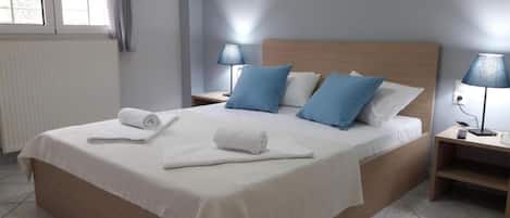 A neatly made bed with white linens and blue pillows, two bedside lamps, and a rolled white towel on the bed.