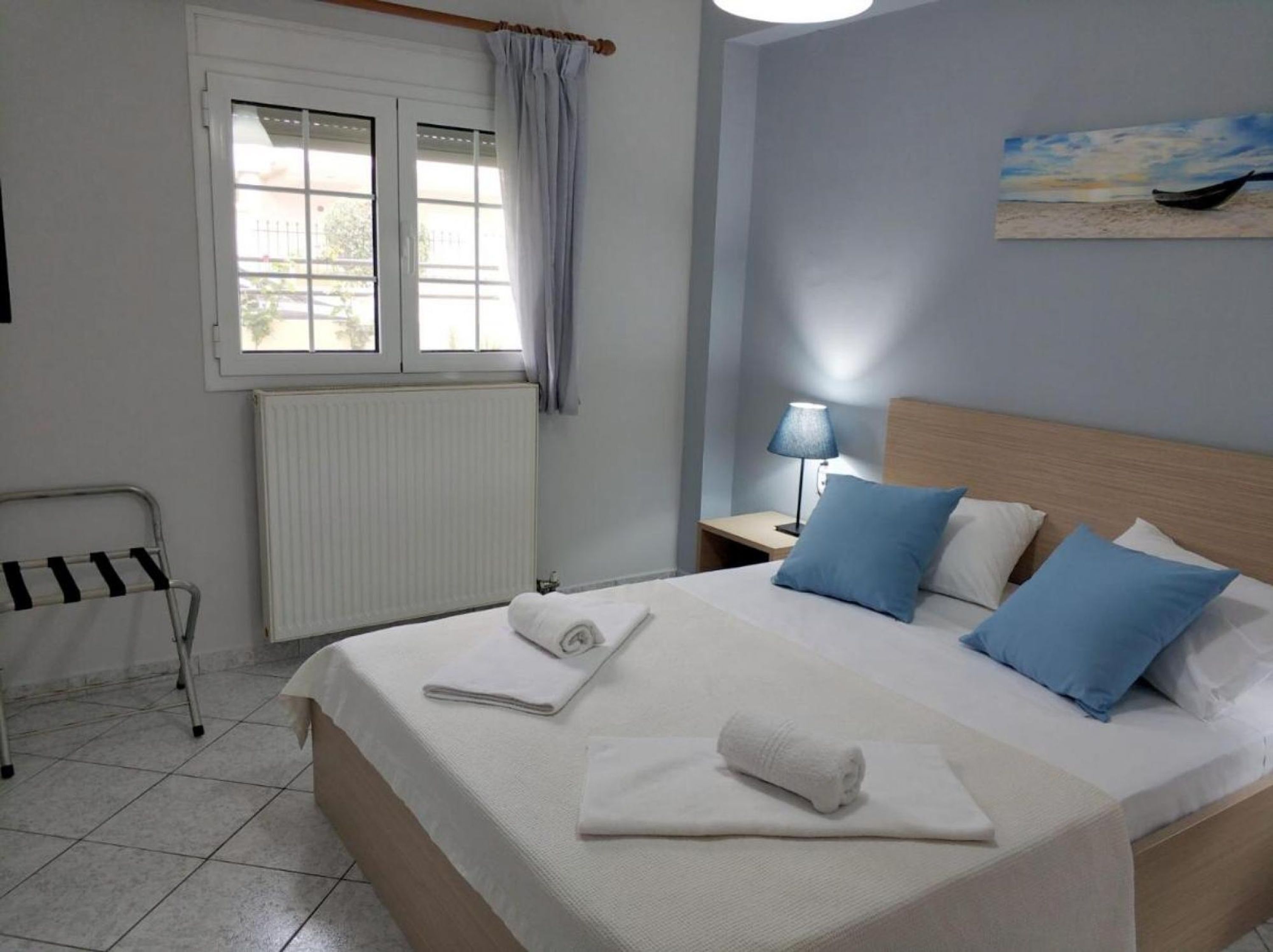 A hotel room with a bed, a nightstand with a lamp, a window with curtains, and a radiator.