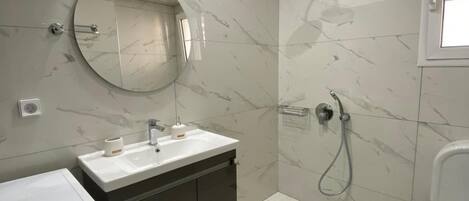 A modern bathroom with a built-in washing machine, a sink, a mirror, and a shower.