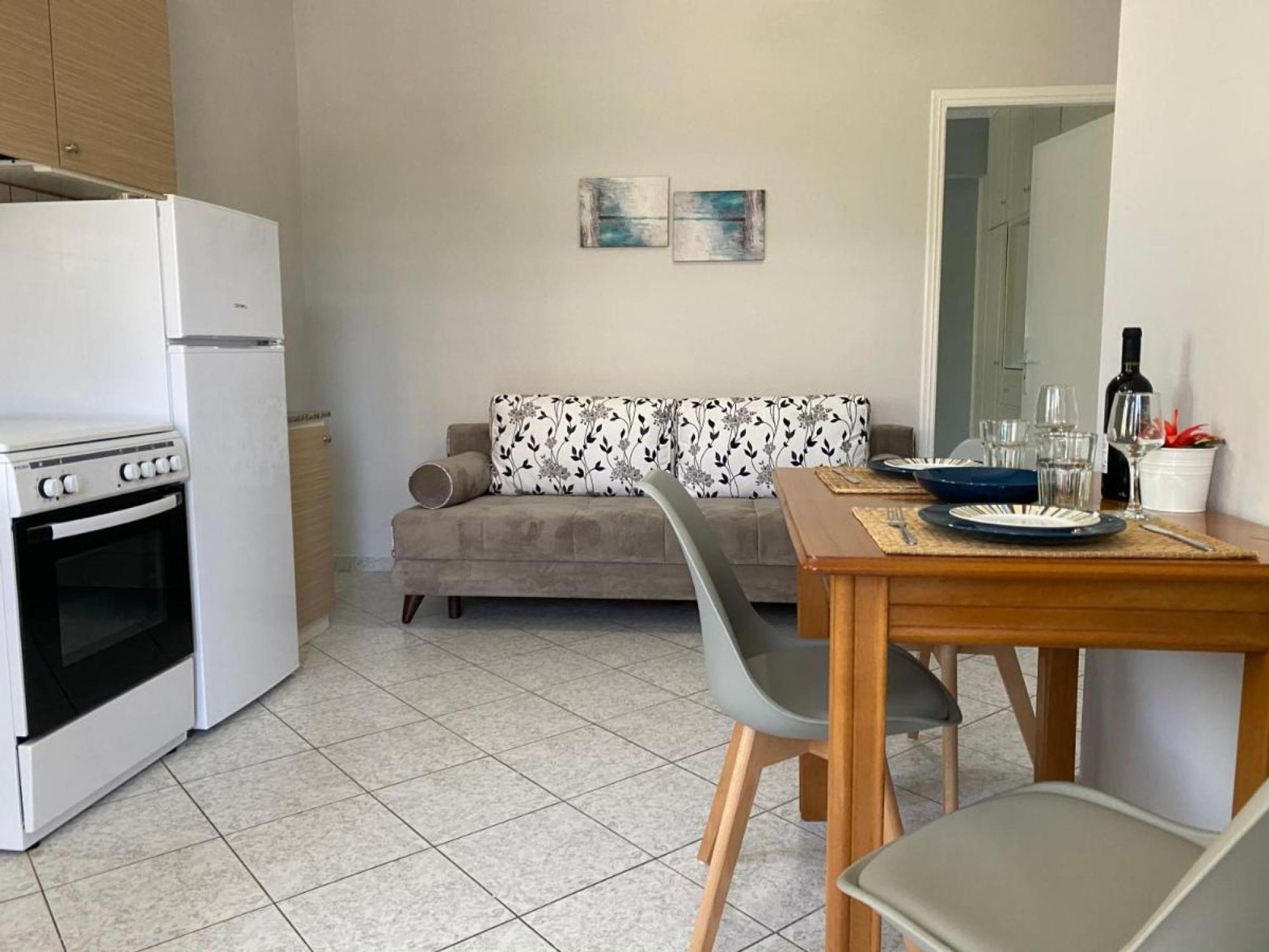 A compact kitchen with a stove, oven, and white refrigerator. A dining table with chairs is set up in front of a sofa with floral cushions.