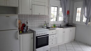 A kitchen with white cabinets, a stove, a sink, and a window with curtains. - Lefkada Blue - Apartments (Lefkada)