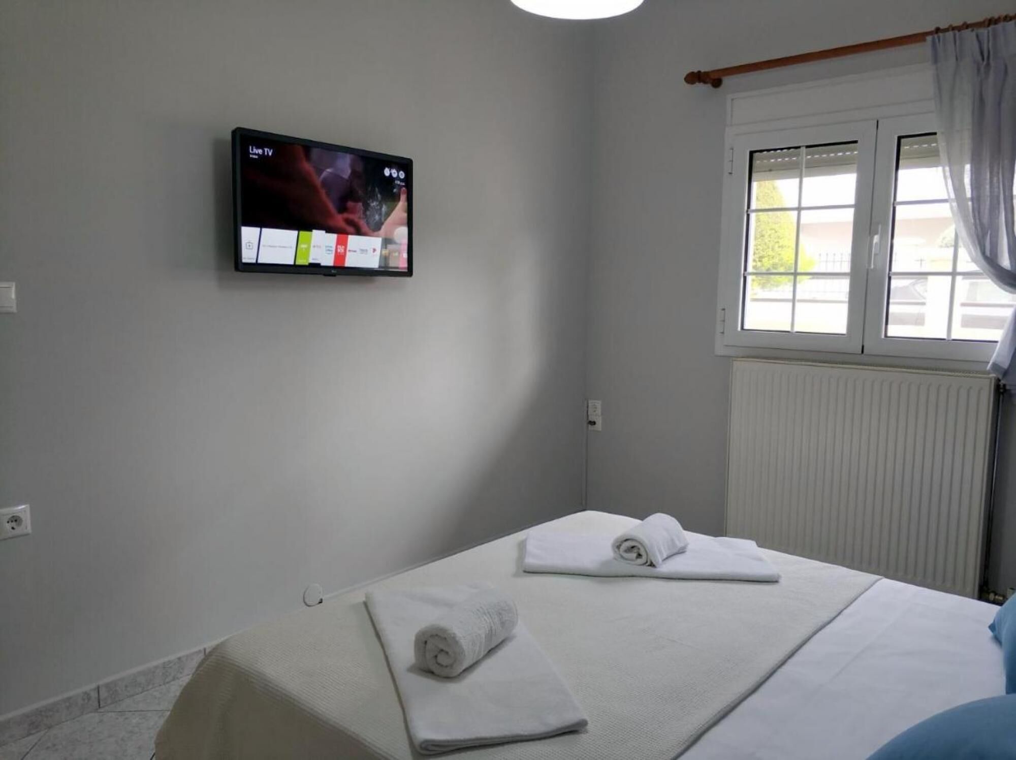 Een hotelkamer met een bed, een aan de muur bevestigde televisie en een raam met gordijnen.