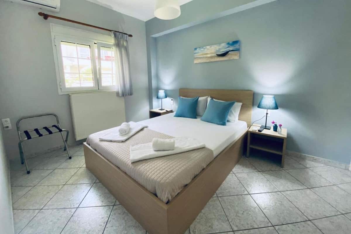 Une chambre avec un grand lit, deux tables de chevet avec des lampes, une fenêtre avec des rideaux, un radiateur et un porte-serviettes.