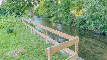 Eine Holzbank an einem Fluss, mit üppigem Grün und Bäumen im Hintergrund.