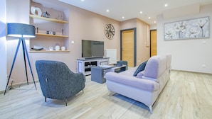 Een moderne woonkamer met een bank, fauteuil, televisie en planken.