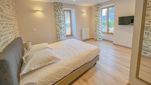 Een slaapkamer met een groot bed, twee ramen met gordijnen, een radiator en een stenen muur.