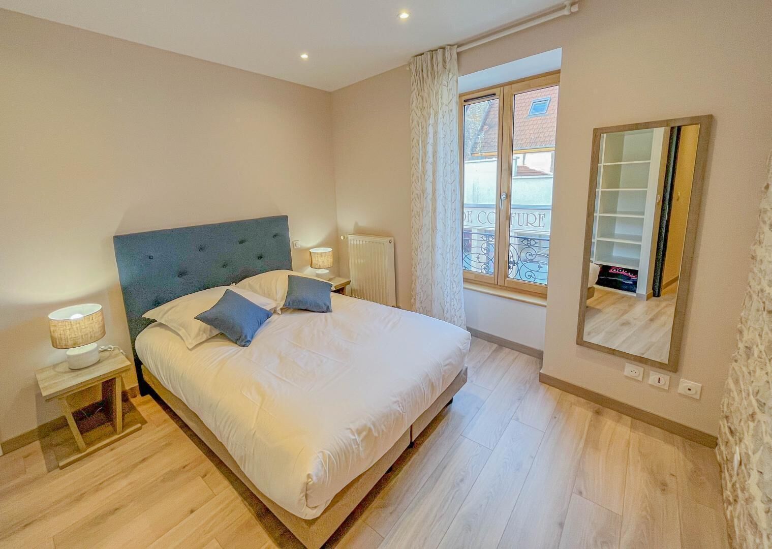 A bedroom with a large bed, two bedside lamps, a window with a view, and a mirror on the wall.