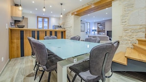 Een moderne eethoek met een glazen tafel en grijs gestoffeerde stoelen, houten details en stenen muren.