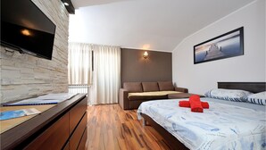 Ein modernes Hotelzimmer mit einer Wand aus Steinimitat, einem Flachbildfernseher, einer Schlafcouch, Holzboden und einem Bett mit blumentückigem, blauem Überwurf.