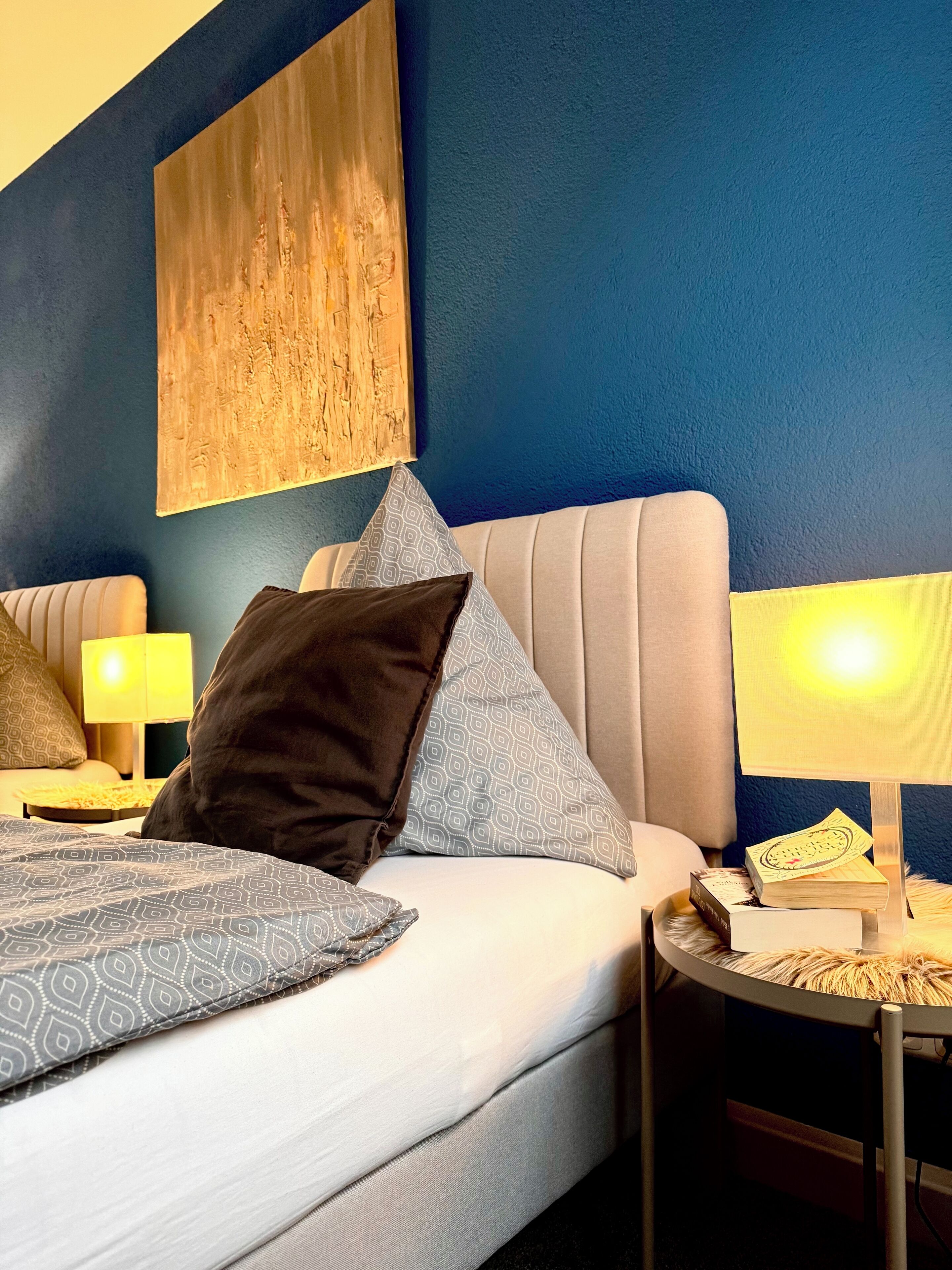 A modern hotel room with a large bed, two bedside tables with lamps, and a large abstract painting on the wall.