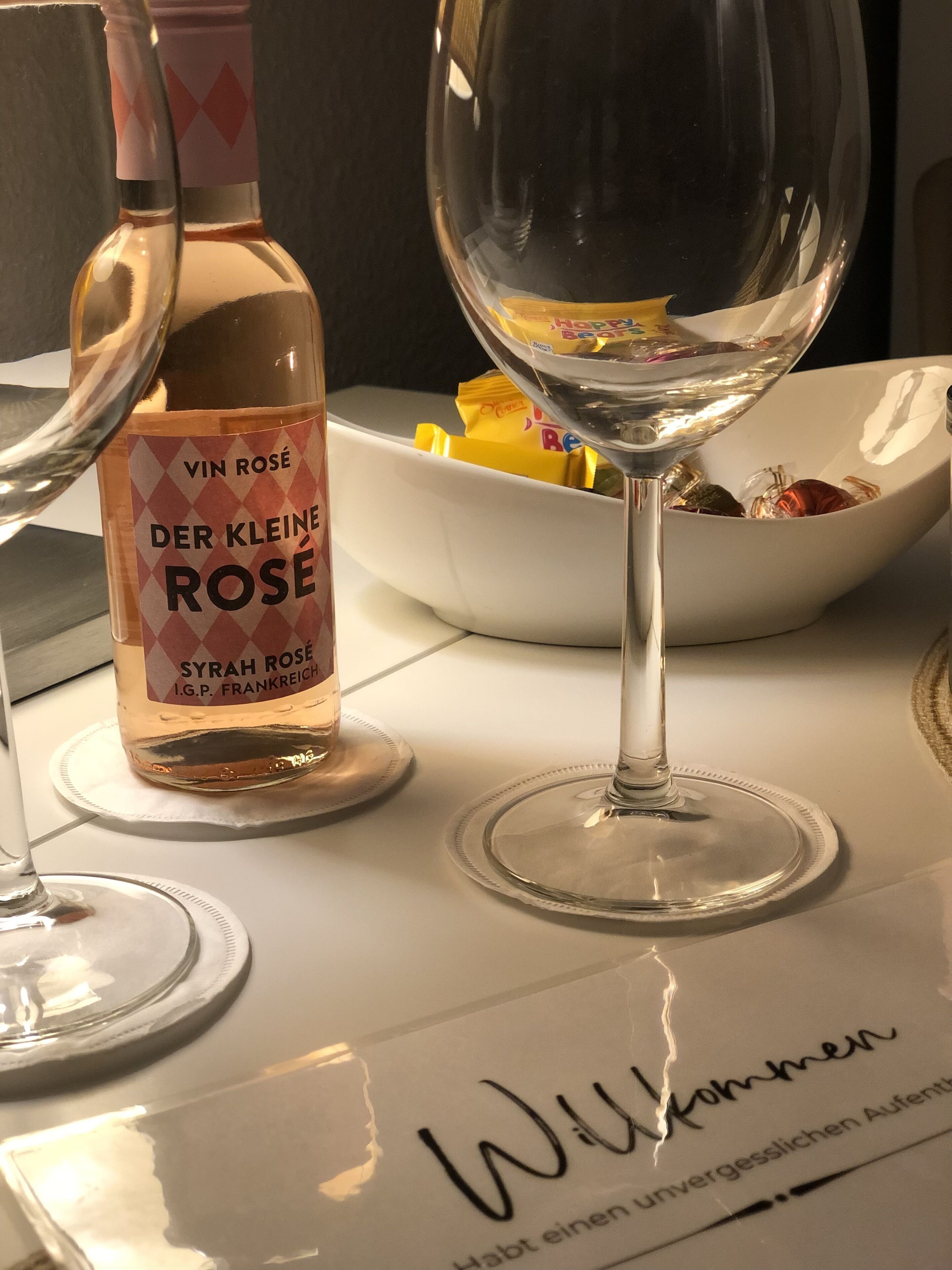 Eine Flasche Der Kleine Rose Wein und ein Weinglas auf einem Tisch mit einer Schale Snacks.