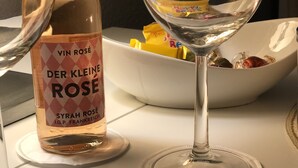Eine Flasche Der Kleine Rose Wein und ein Weinglas auf einem Tisch mit einer Schale Snacks.