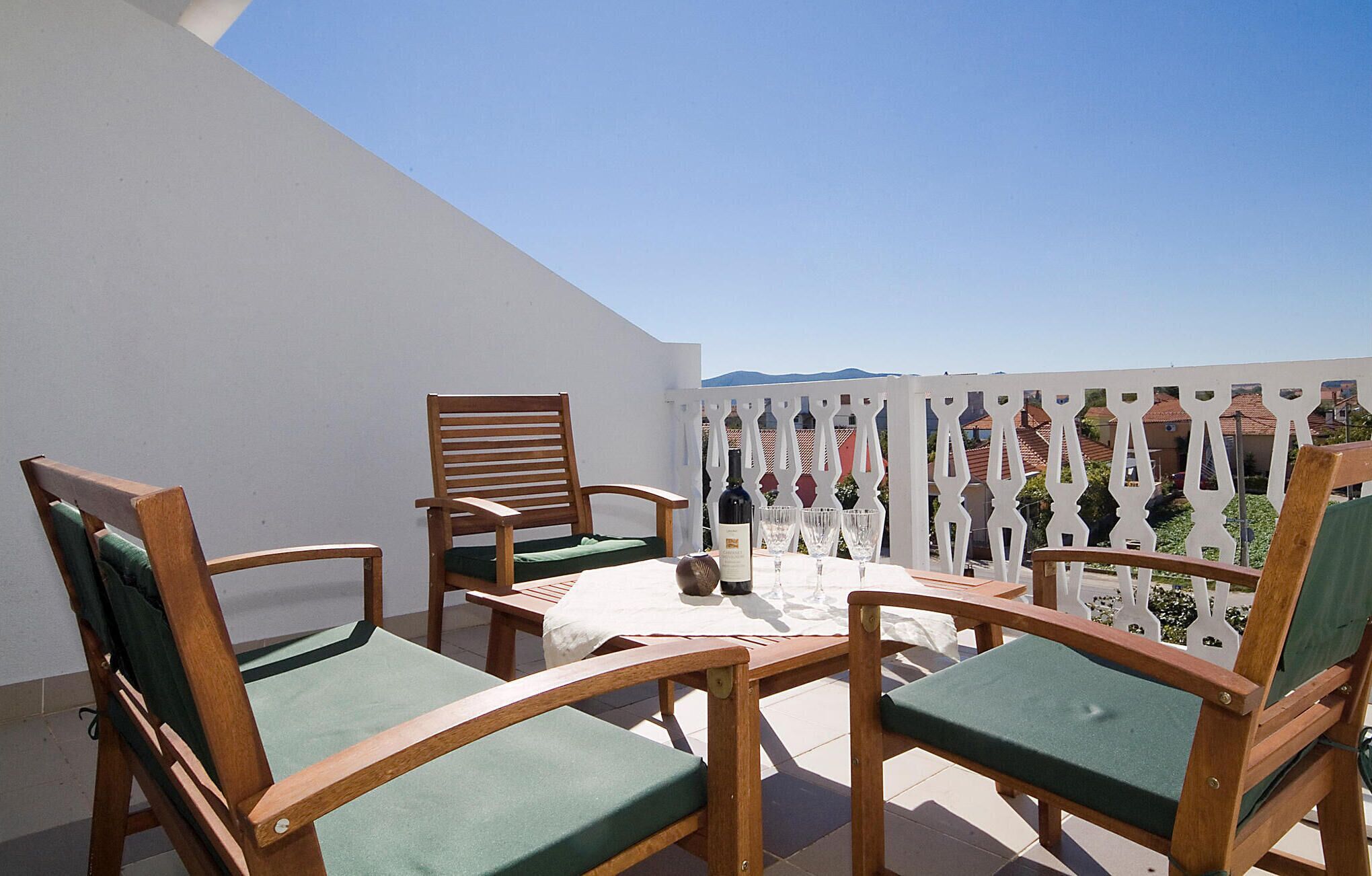 A terrace with wooden chairs and a table, white railing, and a clear view of the surrounding area.