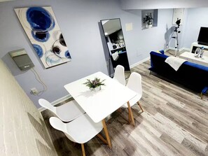 A modern living room with a white table, two white chairs, a blue sofa, a large mirror, and a camera on a tripod.