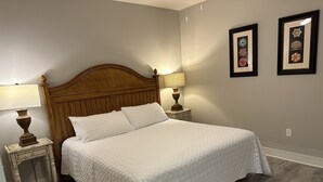 A neatly made bed with a wooden headboard, two bedside tables with lamps, and framed artwork on the wall. - Cozy beach condo with many amenities for fun and relaxation conveniently located (Orange Beach)