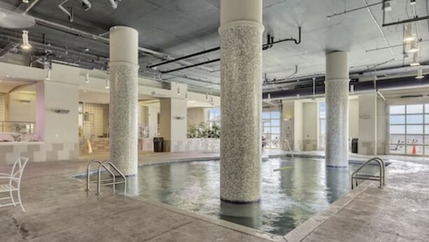 An indoor swimming pool with stone columns, a concrete floor, and a view of the outside. - Cozy beach condo with many amenities for fun and relaxation conveniently located (Orange Beach)