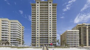 A high-rise hotel with multiple balconies, located on a beach with a clear sky. - Cozy beach condo with many amenities for fun and relaxation conveniently located (Orange Beach)