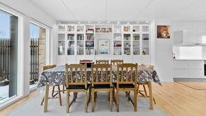 A dining area with a table set for six, surrounded by wooden chairs with floral upholstery. Behind the table is a white shelving unit filled with books, decorative items, and kitchenware. - Awesome home in Nivå with WiFi (Nivå)