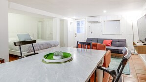 Quarto moderno e bem iluminado, com mesa de jantar, sofá e cama.