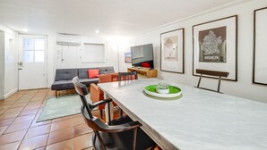 Uma sala de jantar com uma mesa comprida, cadeiras, uma televisão e quadros nas paredes.