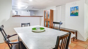 Uma área de refeições com mesa de mármore branco, quatro cadeiras e um banco, além de um tabuleiro verde.