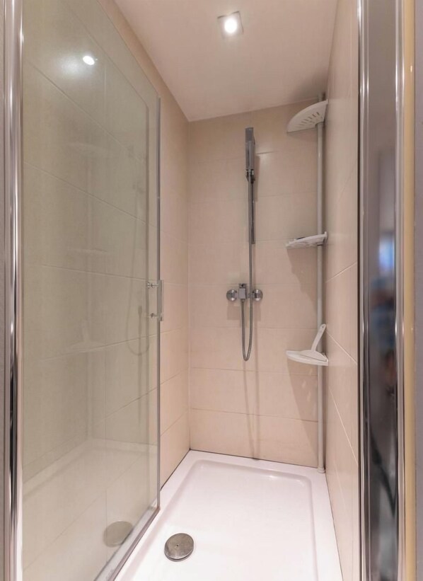 A glass-enclosed shower stall with a handheld showerhead, a built-in shelf, and a drain. - LE 10 - Volvic - Gîte (VOLVIC)