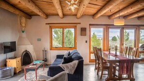 Una sala de estar acogedora con chimenea, un sofá, una mesa de comedor y ventanas grandes que dan al exterior.