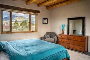 Un dormitorio con cama, tocador, silla y un amplio ventanal con vista a la montaña.