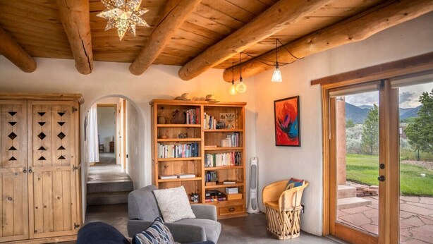 Una sala de estar acogedora con techo de madera, una estantería, una chimenea y un ventanal con vistas al exterior.
