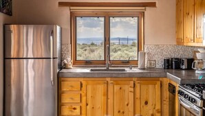 Una cocina con armarios de madera, un refrigerador de acero inoxidable, un lavamanos doble y vistas al exterior.