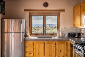 A kitchen with wooden cabinets, a stainless steel refrigerator, a double sink, and a view of the outdoors. - Casa Lobo - Wild Relaxation - Private Hot Tub (El Prado)