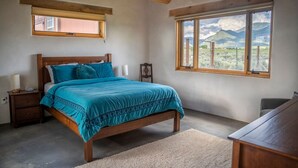 Un dormitorio con cama, mesita de noche, cabecera de madera, ventana con vista a la montaña y techo de madera.