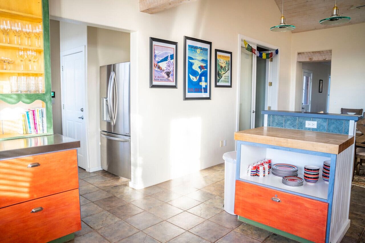 A kitchen with a refrigerator, a sink, and a countertop with dishes. There are three framed pictures on the wall.