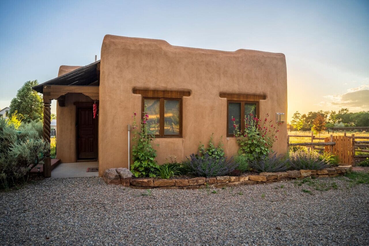 Une maison rustique en adobe, avec une porte en bois, deux fenêtres et une allée gravillonnée.